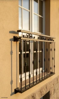 Klasický francúzsky balkón s krútenými tyčami na okne domu s pieskovou fasádou